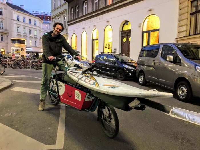 Mit einem Grätzlrad Transportfahrrad wird ein Surfbrett transportiert.