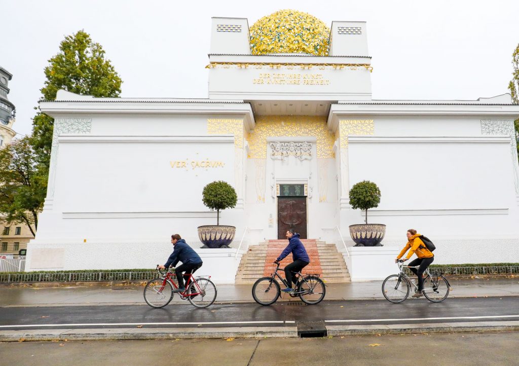 Drei Radfahrende radeln auf dem Radweg vor der Secession.