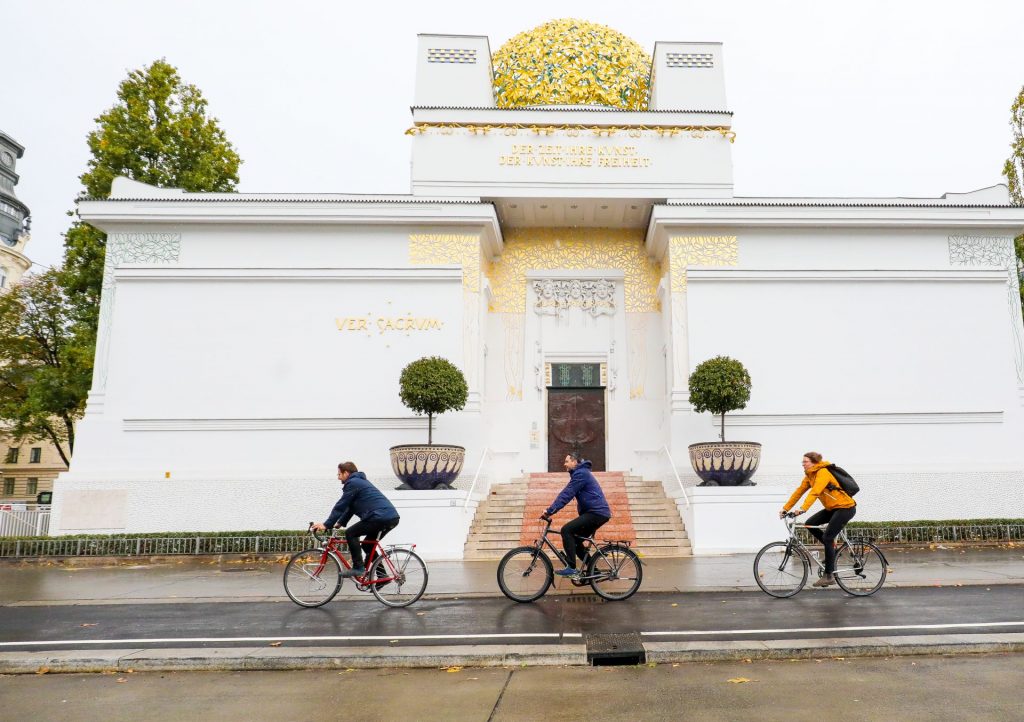 Drei Radfahrende radeln auf dem Radweg vor der Secession.