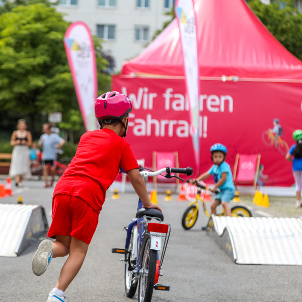 kinder laufen und fahren mit dem Fahrrad zwischen kleinen Rampen und bunten Hütchen herum.